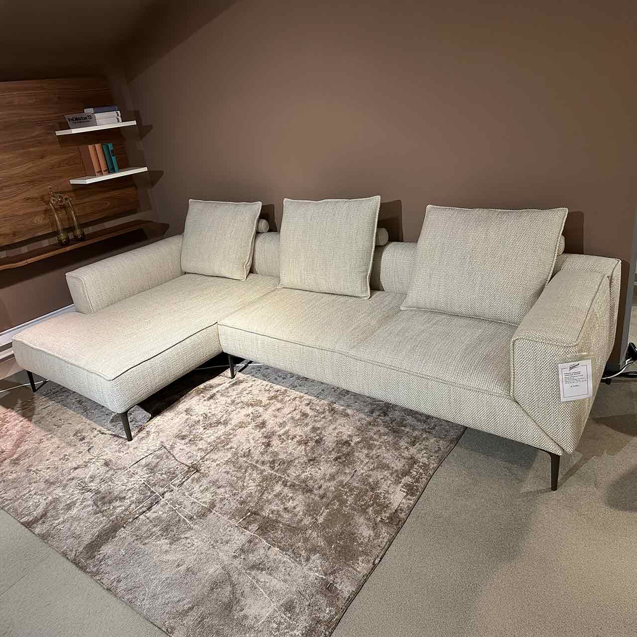 Helles modernes Ecksofa mit Ottomane links und Stoffbezug in Beige mit drei Rückenkissen in gleichem Stoff.