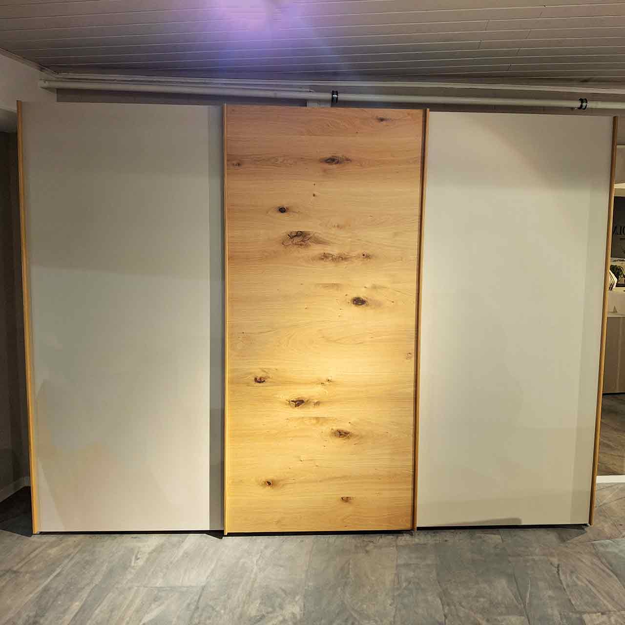 Loddenkemper Schwebetürenschrank Kristallgrau / Balkeneiche Schwebetürenschrank mit drei Türen, Fronten der Türen von links nach rechts: grauer Lack, Eiche mit Maserung, grauer Lack.