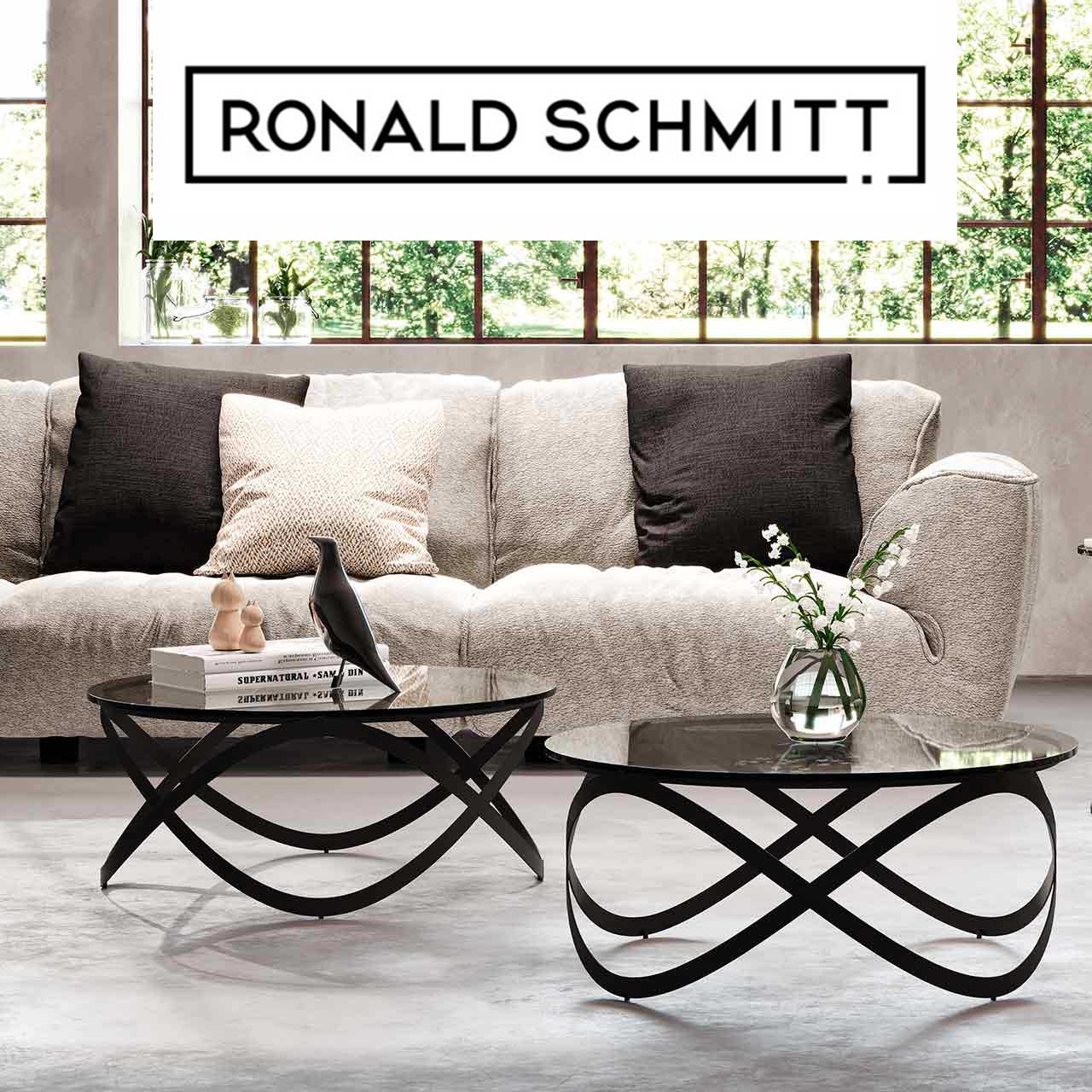 MH_Markenshops_Ronald-Schmitt Ambientebild der Marke Ronald Schmitt mit Designersofa Stoffbezug in Cremeton meliert und zwei schwarzen Coachtischen mit geschwungenem Metallgestellund dunkler Glasplatte.