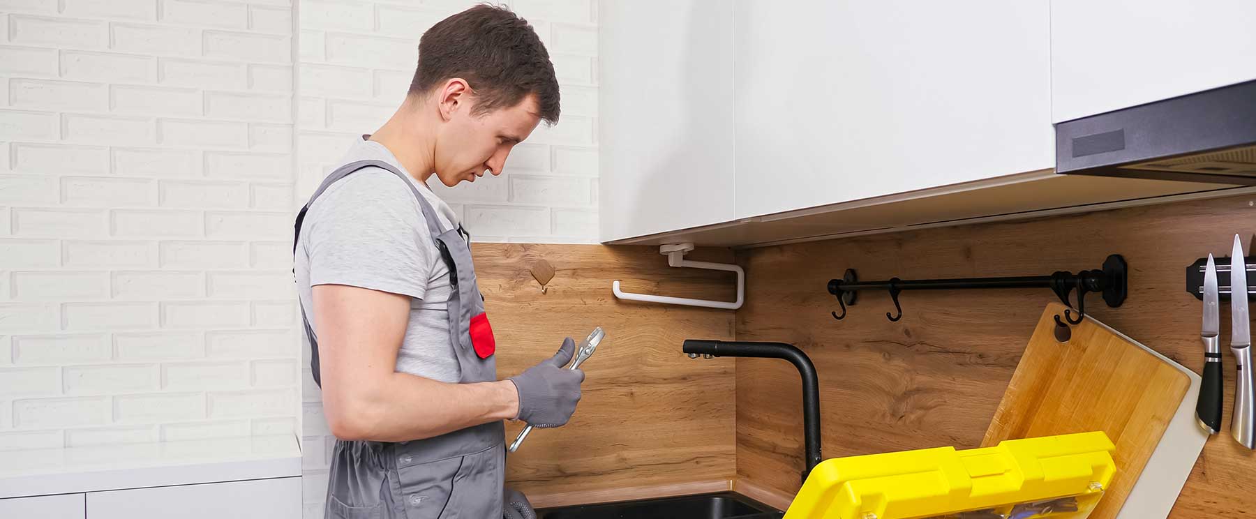 Ein Mann in Arbeitskleidung montiert gerade eine Küche und hält dabei Werkzeug in der Hand