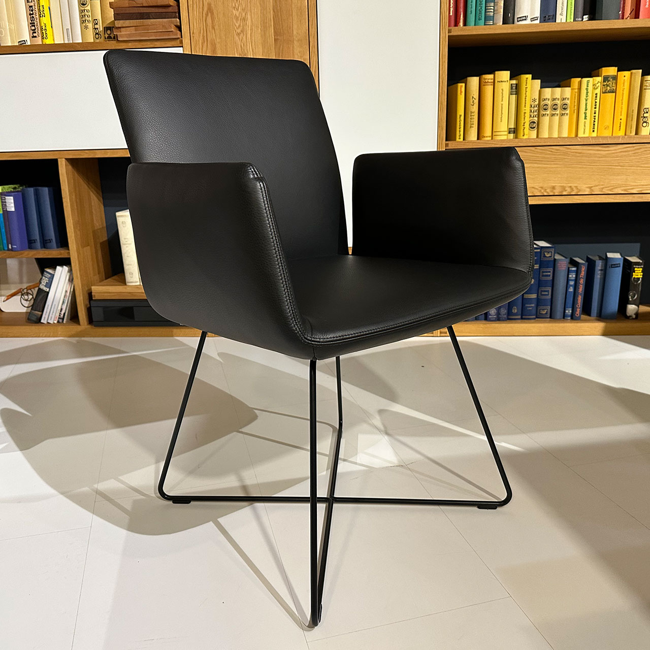 Armlehnstuhl aus schwarzem Leder mit hochgebogenen Armlehnen und überkreuztem Drahtgestell.