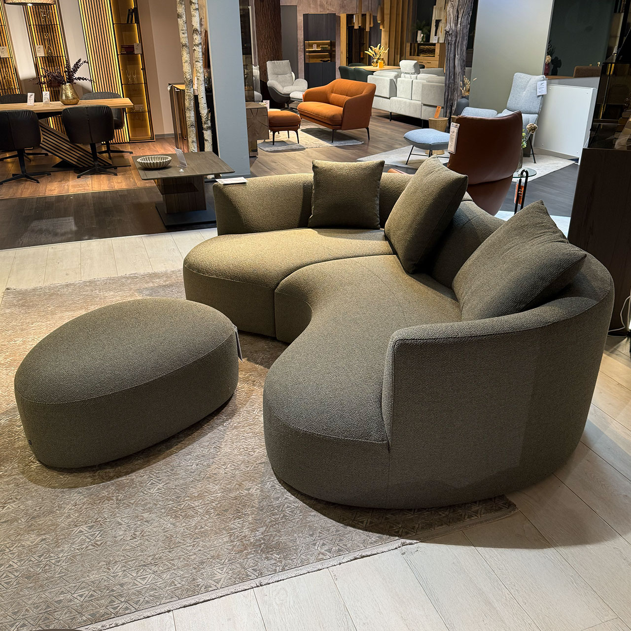 Organisch geformtes Sofa mit drei Kissen und organischem Hocker davor