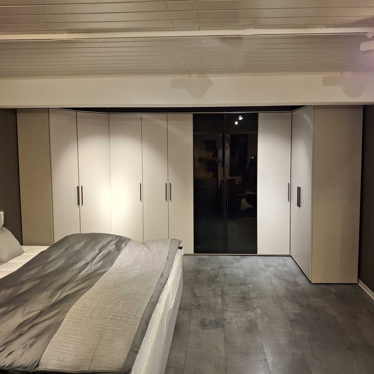 Loddenkemper - Eckkleiderschrank Kristallgrau Überblick Kleiderschrank mit zwei Eckelementen in Kristallgrau (fast weiß). Links Eckelement mit zwei Türen, an der Hauptfläche drei Türen mit Holzfront, zwei Türen mit dunkler Glasfront, dann wieder ein Eck-Element mit einer Tür und einer Falttür.