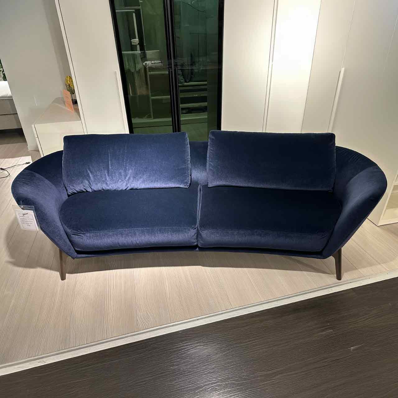 Sofa mit zwei Kopfkissen und abgerundeten Armlehnen aus glänzendem leuchtend blauem Stoff.
