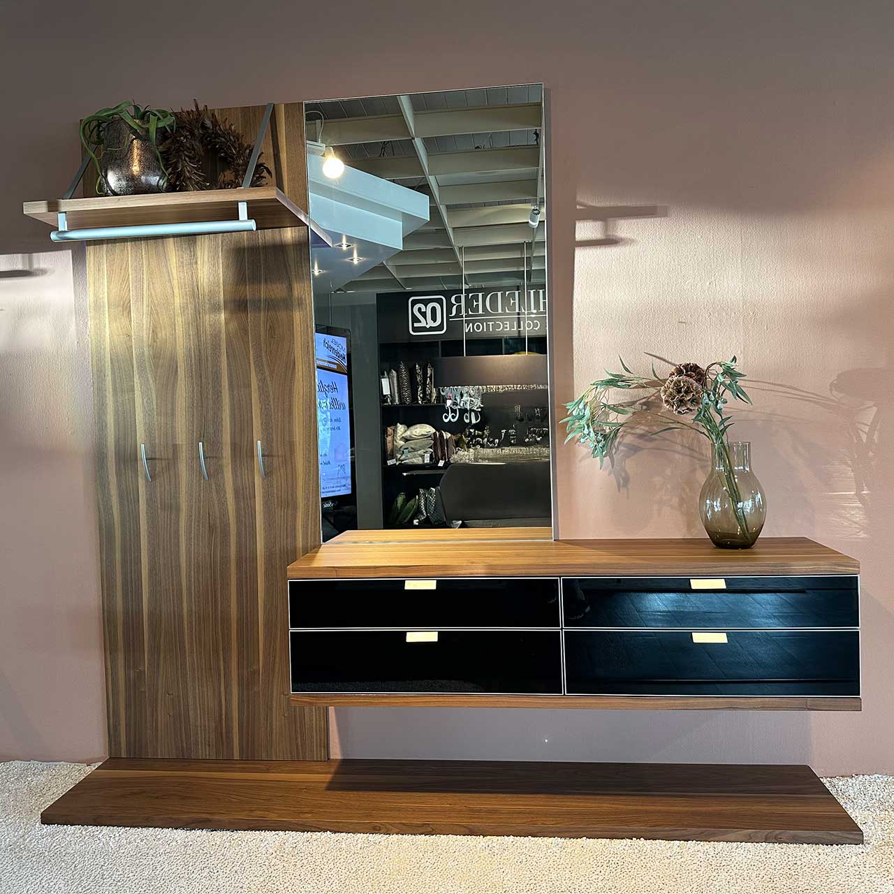 Hülsta - Garderobe Tameta Garderobe aus dunkel gemasertem Holz. Links Garderobenpaneel mit Hutablage, Kleiderstange und Taschenhaken. Rechts daneben Hängekommode mit vier Schubladen mit glänzender schwarzer Front. Darüber ein Spiegel.