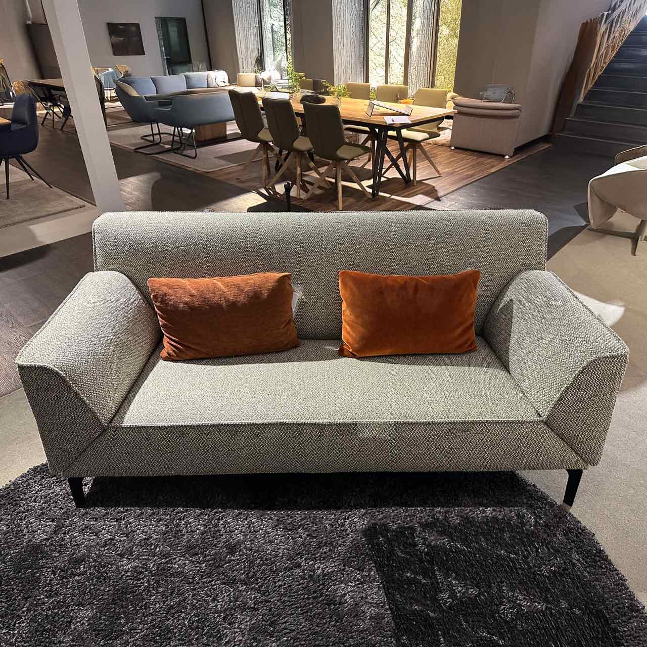 Zweisitzer-Sofa mit hochgeklappten Armlehnen auf schlichten schwarzen Füßen. Auf dem Sofa liegen farblich rotbraune Kissen als Farbkontrast.