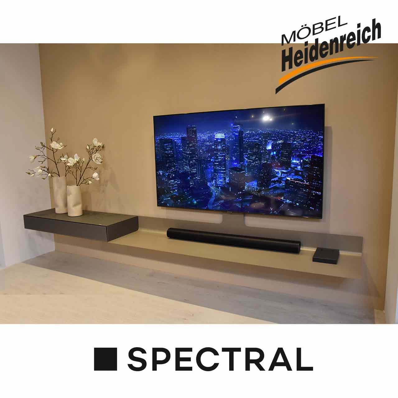 Spectral - Hängelowboard Air Schmale lange hellgraue Ablage mit links einer dunkelgrauen Kästchen mit Klappe. Daran montiert ein großer Fernseher.Auf der Ablage liegt ein Sonos-Gerät.