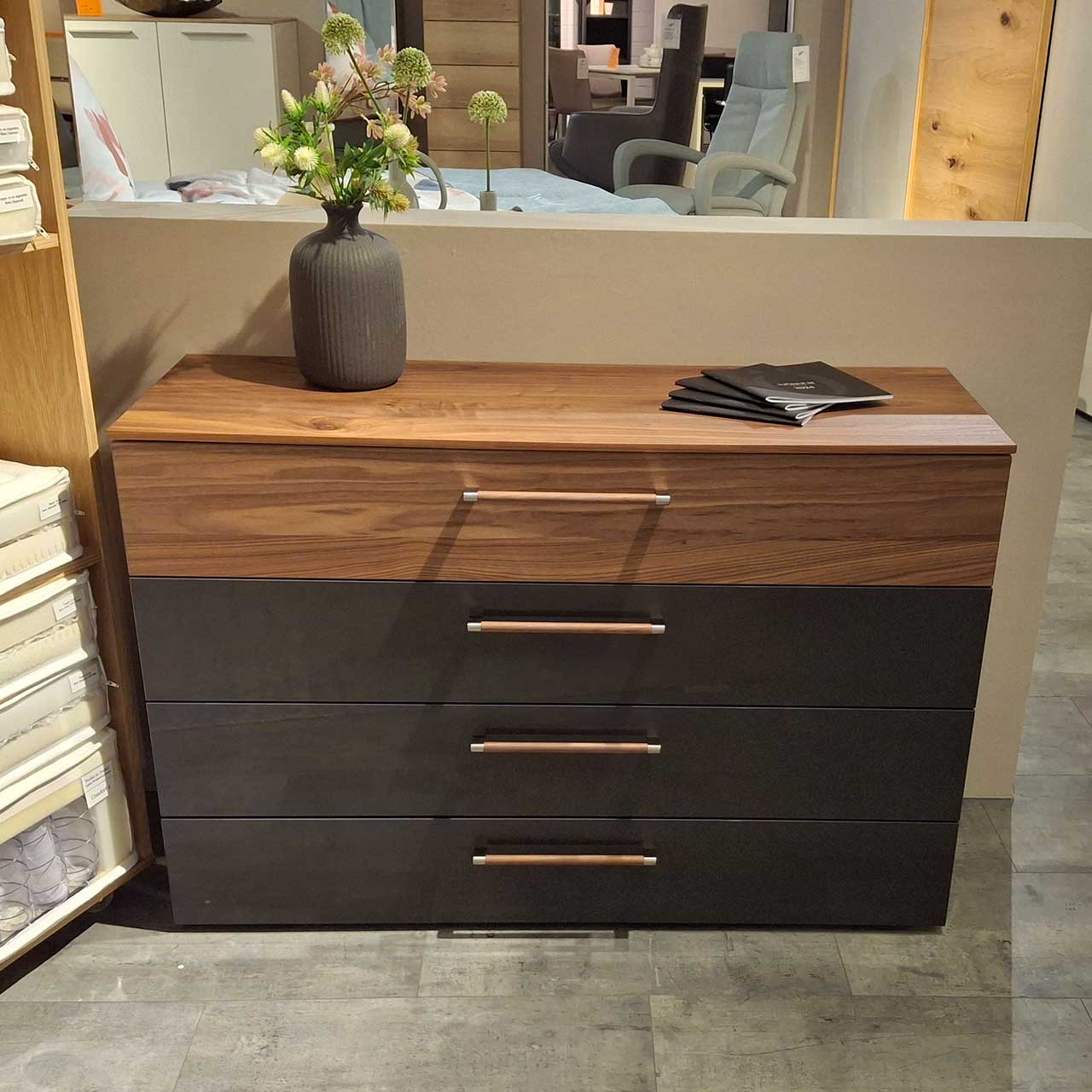 Loddenkemper Kommode 600 Grau Nussbaum Kommode mit 4 Schubladen. Obere Schublade und Abdeckplatte Holz mit Maserung. Untere drei Schubladen Grau. Griffe länglich mit Holz-Ummanteltung.