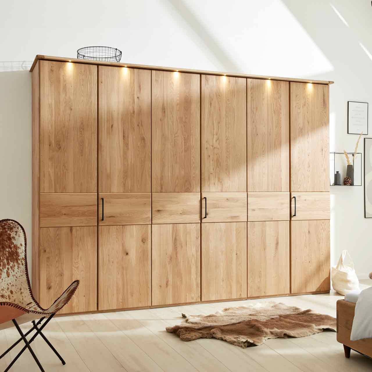 Loddenkemper - Kleiderschrank Eiche 6-türig mit Beleuchtung Kleiderschrank aus hellem Holz mit 6 Türen und Kranz mit Beleuchtung oben. In der Mitte eine durchlaufende optische Absetzung. An jeder zweiten Tür ist ein Griff.