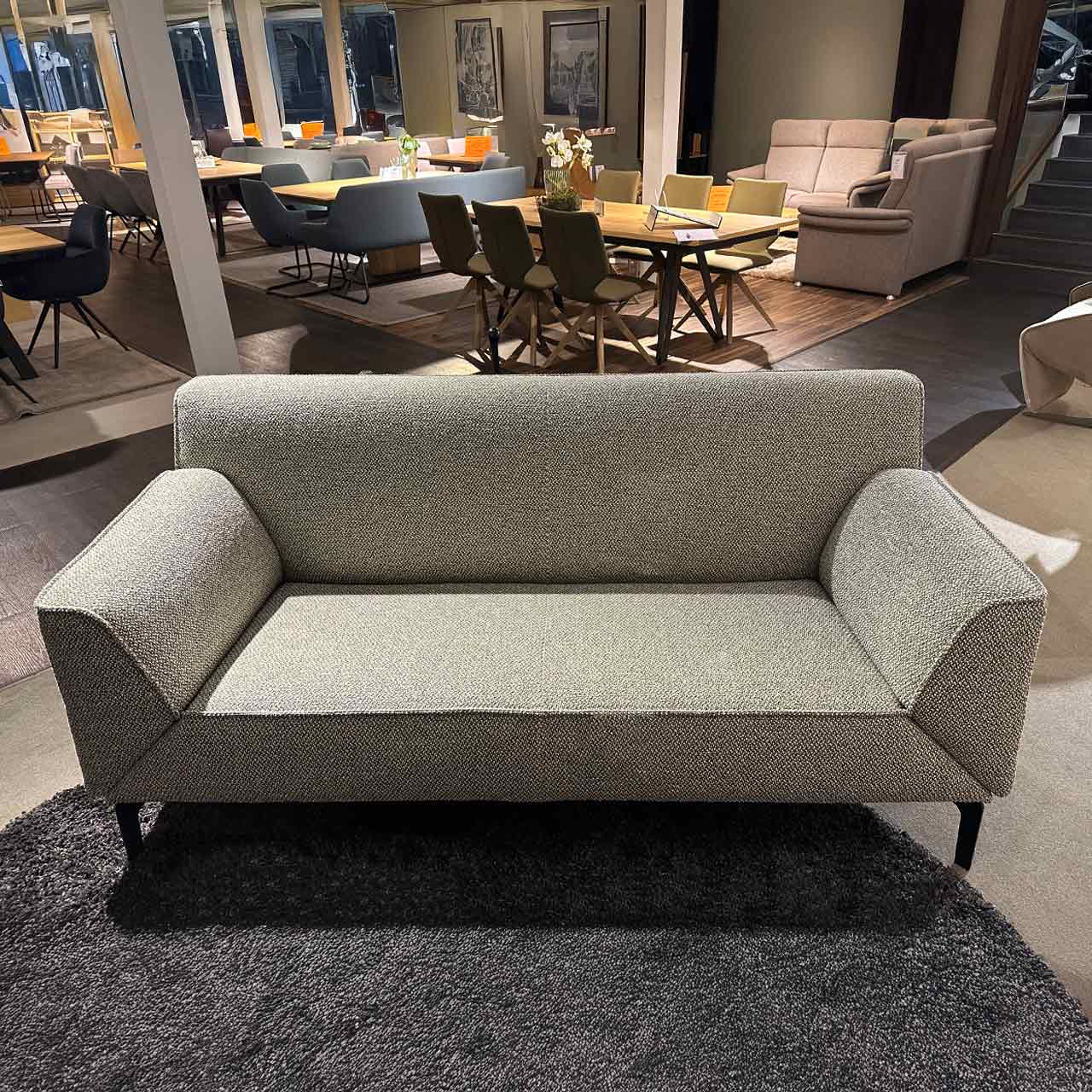 Zweisitzer-Sofa mit hochgeklappten Armlehnen auf schlichten schwarzen Füßen.