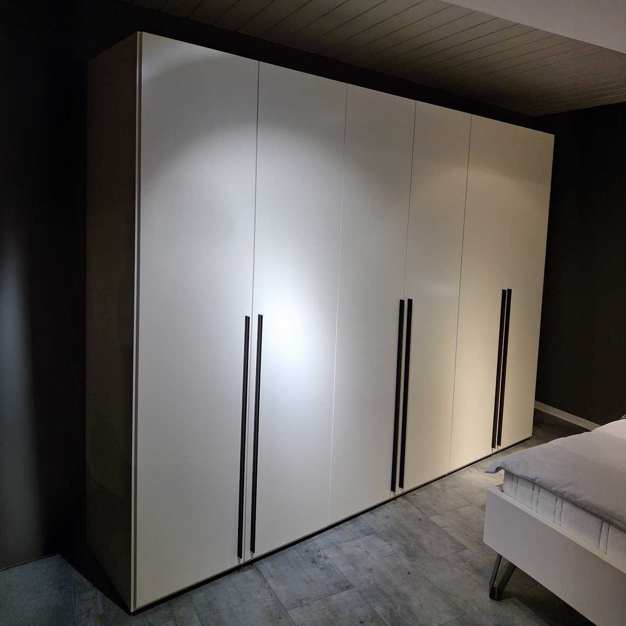 Loddenkemper Kleiderschrank weiß t-türig Weißer Kleiderschrank mit sechs Türen, an denen schwarze Griffstangen befestigt sind.