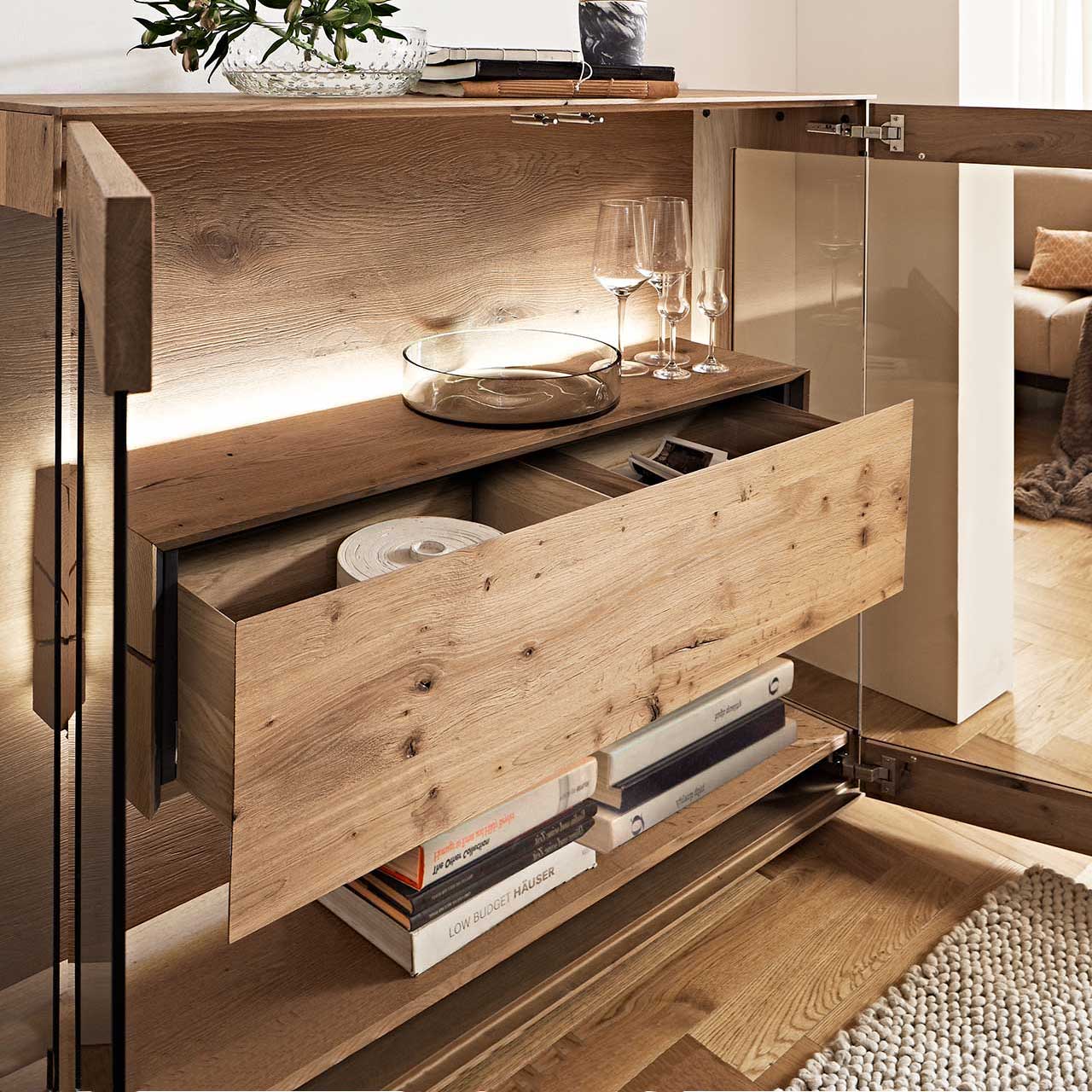 Hartmann CAYA - Highboard 7170-HM-6139 - Detail Doppelschubkasten Geöffneter Doppelschubkasten im beleuchteten Hirnholzblock des Highboards CAYA 7170-HM-6139, mit Einblick in den Stauraum hinter der Parsolbronze-Glastür