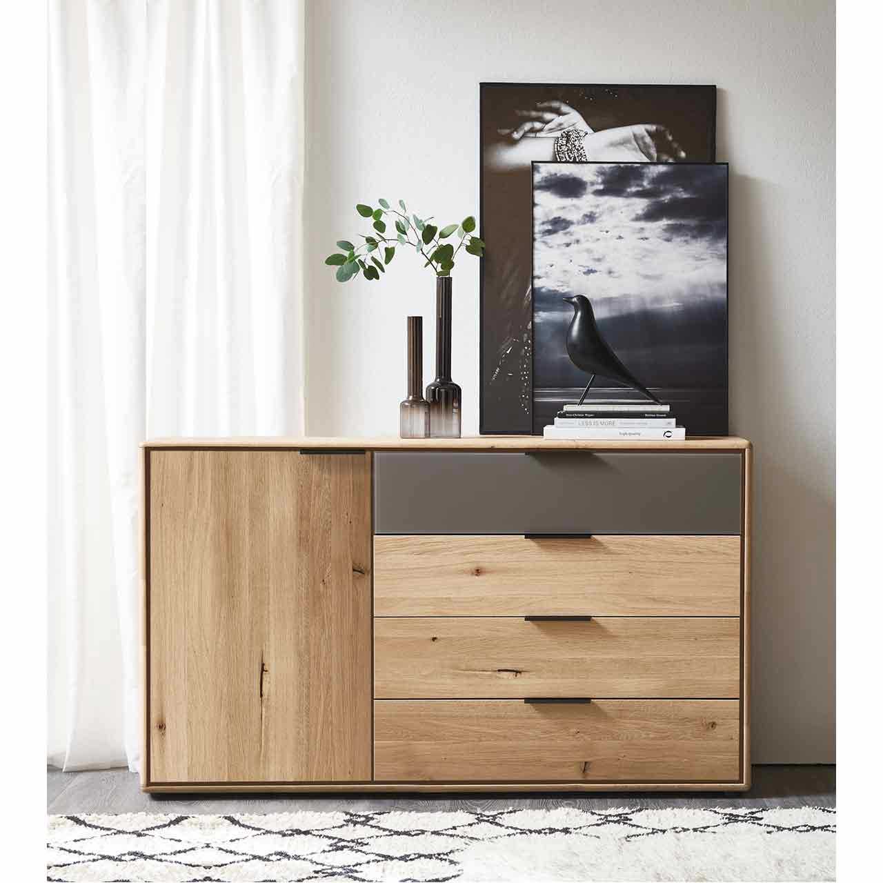 MH_Schlafzimmer_Kommoden Ambientebild mit Fokus auf ein Sideboard / eine Kommode aus Holz mit einer Tür auf der linken Seite und Bier Schubladen auf der rechten Seite. Die oberste Schublade ist in anthrazit abgesetzt.