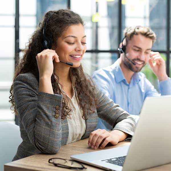 Eine Frau und ein Mann sitzen mit Headsets vor einem Computer und schauen dabei konzentriert aus.